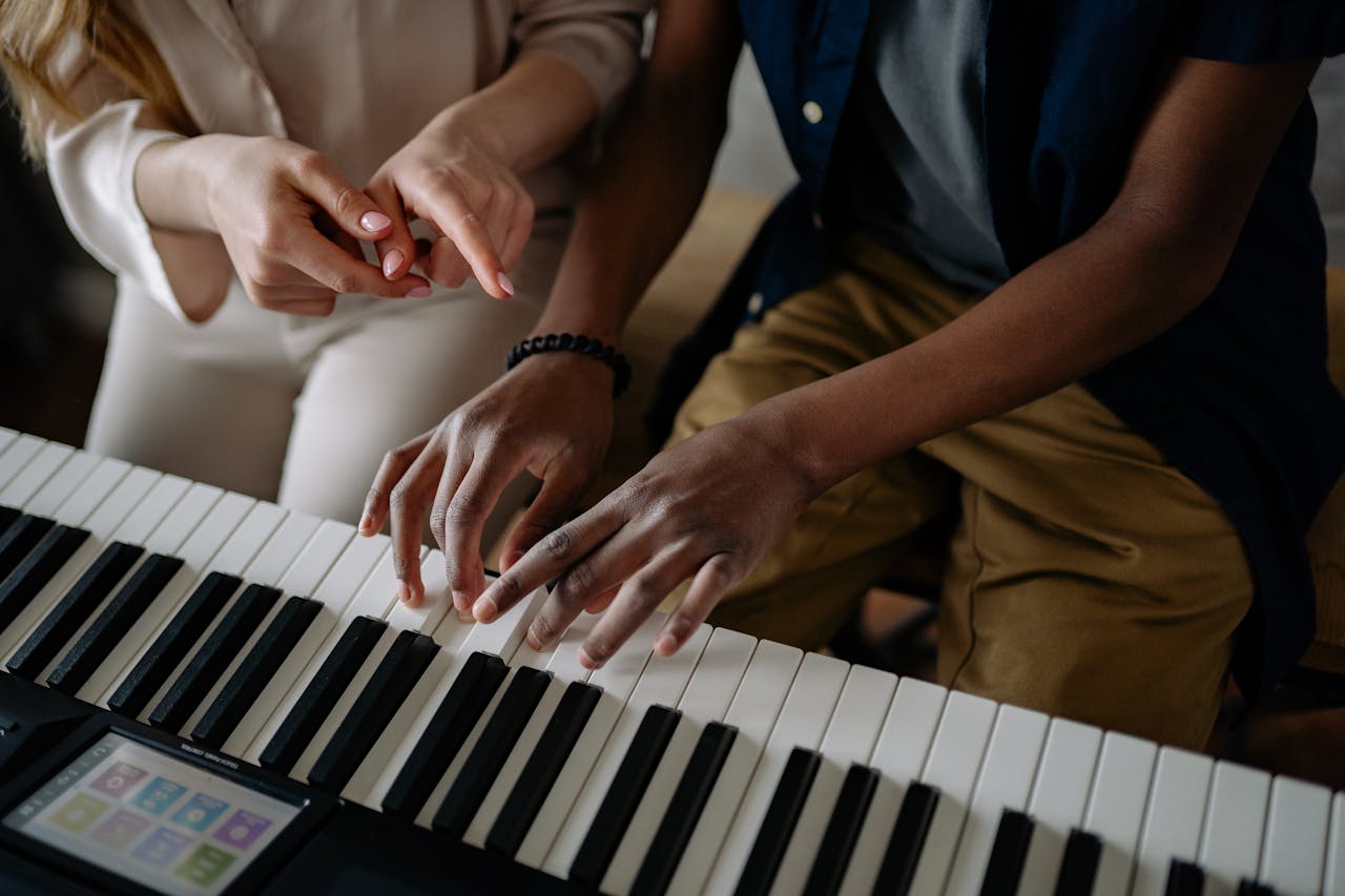Close-up of teacher and student during piano lesson focusing on hand placement.