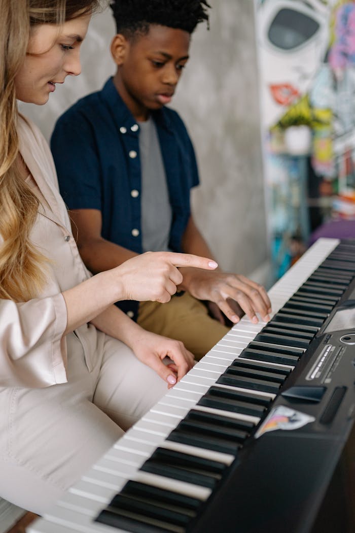 Young boy learning to play the piano with his music teacher at home.